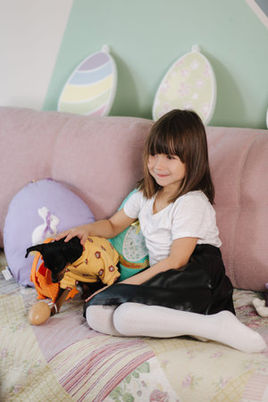 Adorable little girl hug her pet at home on sofa. Kid preparing for easter at home during...