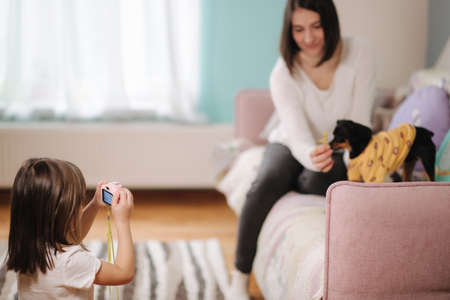 Young daughter photographer make photo of her mom play with dog at home. Toy camera for kidsの写真素材