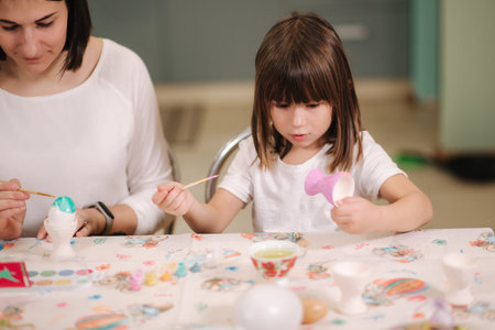 Little girl with her mom preparing for easter and print eggs. They are sitting by the table and have...