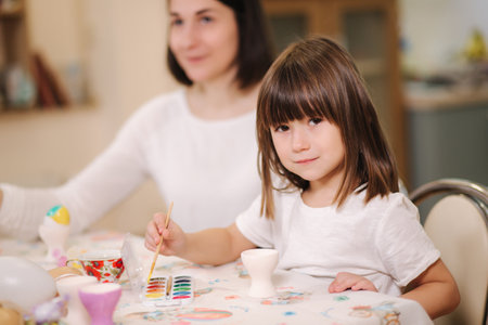 Beautiful daughter spend time with mom at home during qurantine. Cute little girl print on easter eggs with mother. Selebrating spring holidaysの写真素材