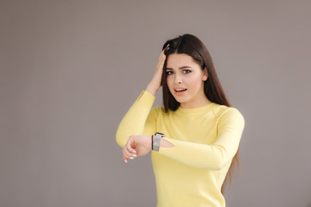 Woman look at the watch and uderstand that she was late. Woman in yellow sweater on grey background.の写真素材