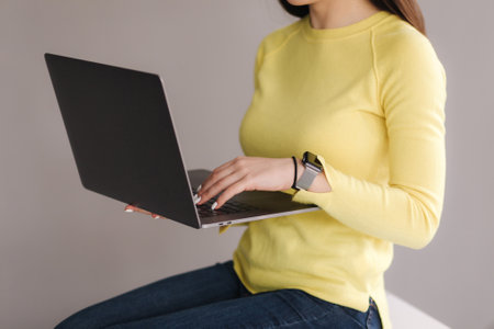 Middle selection of woman in yellow sweatshirt using laptop on gray background. Place for textの写真素材