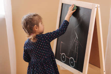 Cute little girl draw on the blackboard at home. Side view of female kid in dress learningの写真素材