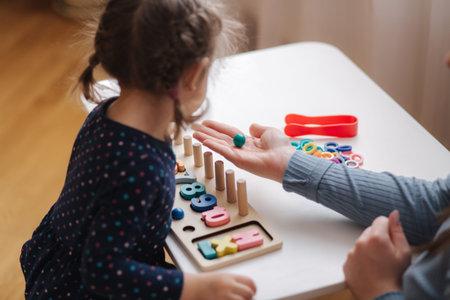 Little girl play in educational game for children with mom. Wooden game with different colors and numbers. Intecactive game for clever kids. Close up of mothers hand give daughter color ballsの写真素材