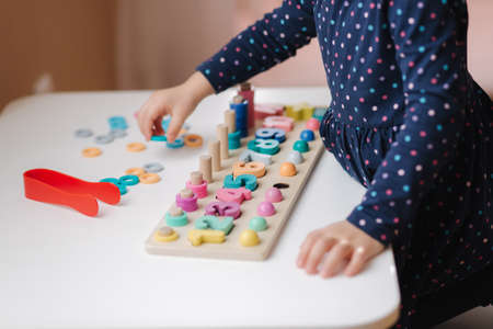 Closeup of kid's hand putting color rings on wooden column. Little girl play in educational game for children at the table. Wooden game with different colors and numbers. Intecactive game for clever kids. At home during qurantine.の写真素材