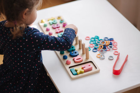 Adorable little girl play in educational game for children at the table. Wooden game with different...