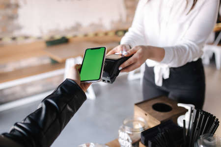 First person view of female paying with smartphone. Cashier hand holding credit card reader machine while client holding phone for NFC payment. Green screen on phone. Mock upの写真素材