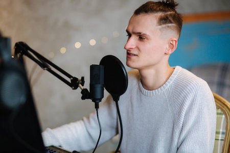 Young man makes a podcast audio recording at home. Man using pc and two professional microphones. Person recording a podcast at home using microphone and computers. Recording online podcastの写真素材