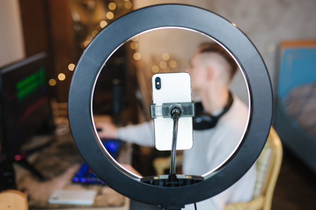 Man recording video on smartphone during the work at home on computer. Young guy recording on...