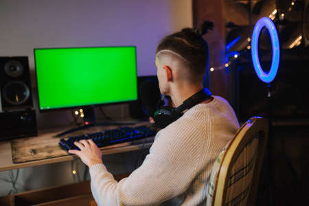 Happy young man in headset with pc computer playing game at home and streaming playthrough. Technology, gaming, entertainment. Chromakeyの写真素材