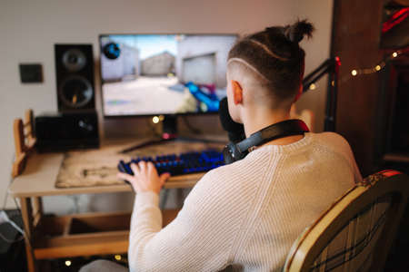 Men playing online video games at home using powerful computer. Streamer man using professional microphone, keypad, mouse in gaming home studio. Back viewの写真素材