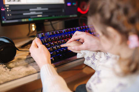 Closeup of little sister help brother and presses button on the keyboard with neon light. Little girl working on computerの写真素材