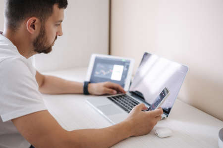 Man looking at finance chart on laptop and tablet, day trader, investing from home. Young man monitors his investments. Ambitious businessmanの写真素材