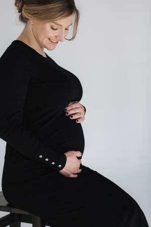 Close up portrait of gogreous pregnant woman in bkack dress hold her hand on belly and looks downの写真素材