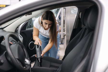 Female using portable vacuum cleaner in her car. Electrical vacuum in womans hand clean car inside...