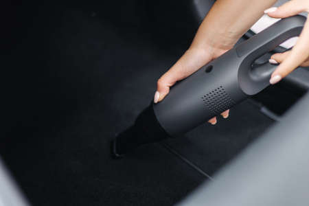 Close-up of woman using portable vacuum cleaner in car. Car interior cleaning. Female vacuuming rug. Dust and dirt removalの写真素材