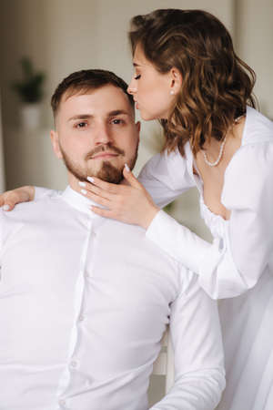 Portrait of young woman kiss husband. Attractive female with her lovely man. White clothesの写真素材