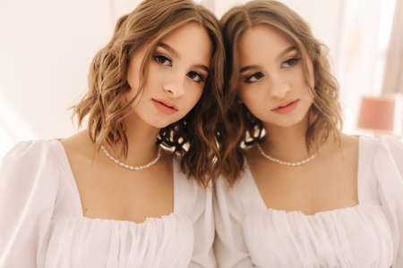 Elegant female model lies near the mirror in with her reflection. Gorgeous and sexy bride in a short dress on the bed strainghtens her hairの写真素材