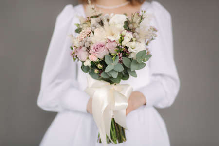 Middle selection of bride hold wedding bouquet in hands. Grey background. Stuio photosessionの写真素材