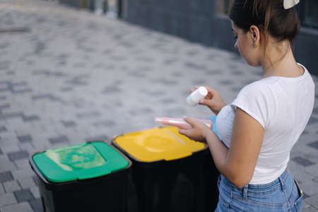 Woman throwing out in recycling bin washed and empty shampoo and deodorant bottles. Female looks at the packages to find out in wich recycling bin throw the garbageの写真素材