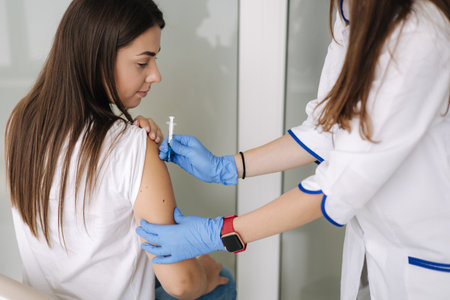 Close-up of doctor in protective gloves holding syringe and using cotton before make injection to patient in medical mask.の写真素材
