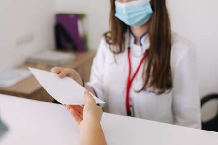 Female doctor in protective mask give paper with recipe to client. Bright clinicの写真素材