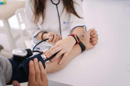 Young man with high blood pressure. Female doctor using sphygmomanometer with stethoscope checking...