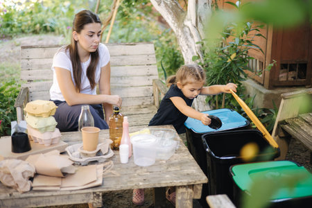 Young mom with her little daughter preparing for recycling different kind of rubbish and putting...