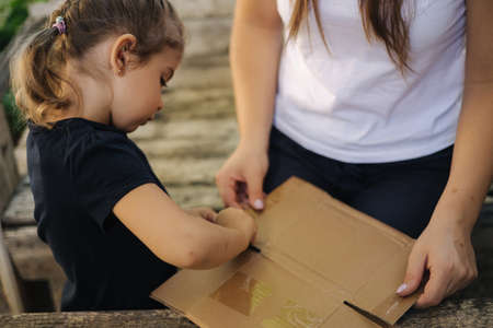 Close-up of little girl with her mom preparing cardboard for recycling. Family sorting garbage at home. Concept of recyclingの写真素材