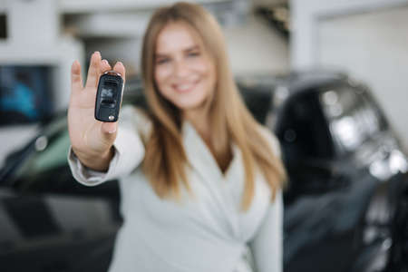 Photo of attractive and young business woman in car showroom. Female hold keys from her new car. Keys in focusの写真素材