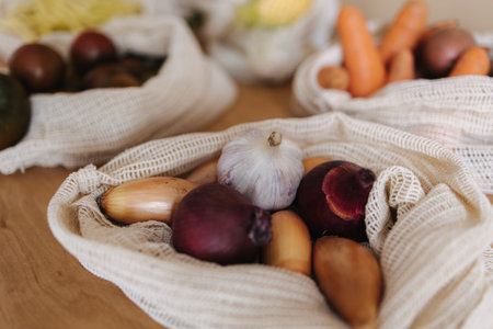 Garlic and onionin reusable grocery bag on a table at home. Mesh cotton with vegetables