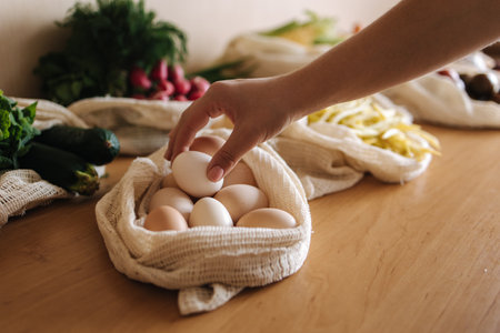 Female hand take egg from canvas grocery bag. Vegetables in reusable eco cotton bags on wooden table. Zero waste shopping concept. Plastic free itemsの写真素材