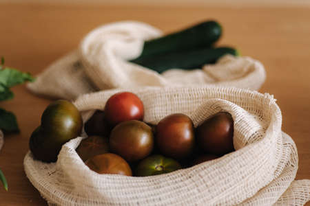 Tomato in canvas grocery bag. Vegetables in reusable eco cotton bags on wooden table. Zero waste shopping concept. Plastic free itemsの写真素材