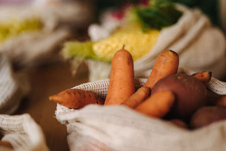 Carrot and potatoes canvas grocery bag. Vegetables in reusable eco cotton bags on wooden table. Zero waste shopping concept. Plastic free itemsの写真素材