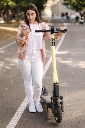Young woman connect an electric scooter outdoors. Woman using phone for contactless payment....