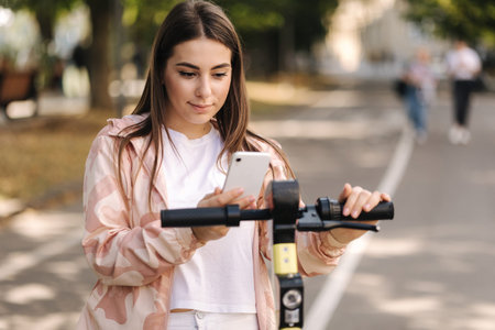 Young woman connect an electric scooter outdoors. Woman using phone for contactless payment....