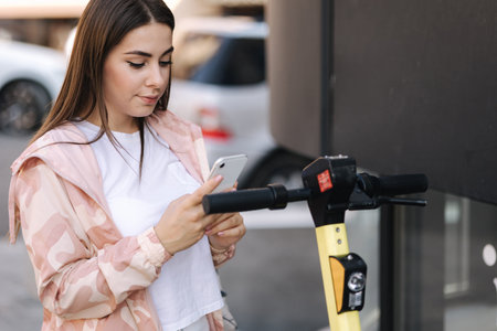 Young woman connect an electric scooter outdoors. Woman using phone for contactless payment....