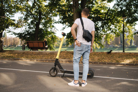 Back view of man with black shoulder bag take his phone from back pocket to connect an e-scooter