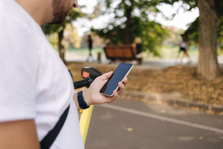 Close-up of hamdsome man using phone during the break befour riding on e-scooterの写真素材