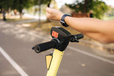 Hand of man connect an electric scooter outdoors. Woman using smart watch for contactless payment. Ecological transportation conceptの写真素材