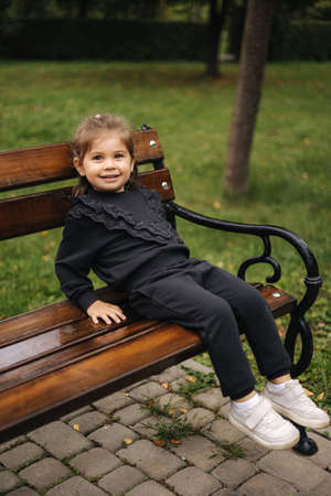 Cute little girl in beautiful black suit sitting on the bench. Autumn moodの写真素材