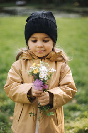 Happy smiled little girl plucked autumn flowers. Beautiful daughter in autumn forestの写真素材