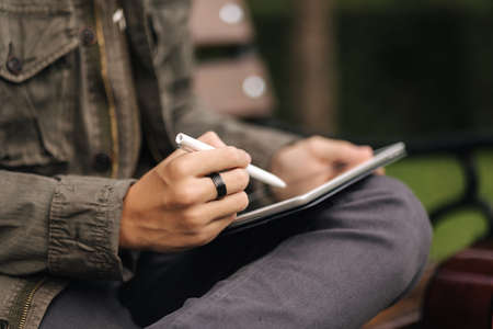 Close-up of boy painting in tablet using pencil. Young designer using tablet outdoor. Autumn timeの写真素材