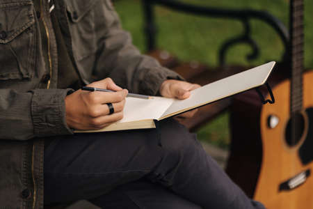 Talanted person is talanted in everything. Teenager writes lyrics for a song. Boy using acoustic guitar. Outdoor in autumn timeの写真素材