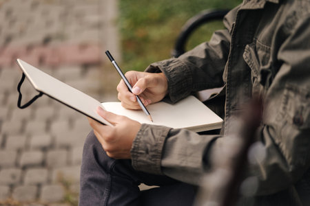 Handsome teenager painting something in his notepad outdood during the break. Talanted young boyの写真素材