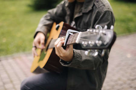 Handsome teenage playing acoustic guitar with capo. Boy sitting on bench and playing musicの写真素材