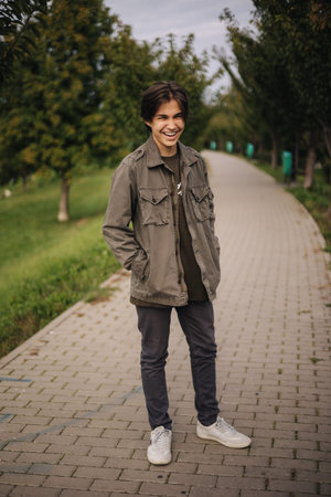 Happy teenage boy walking outdoor in the park in autumn time. Boy in khaki jacket