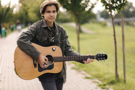 Concentrated teenage boy musician playing acoustic guitar outdoor. Handsome boy love misucの写真素材