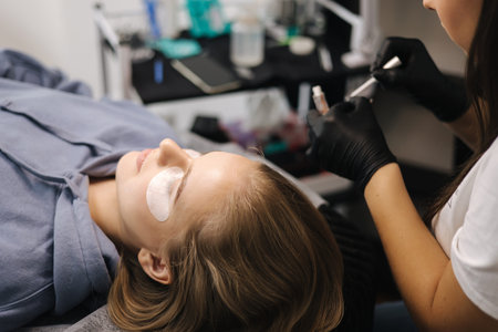 Woman doing eyelashes lamination in beauty studio. Blond hair model has staining, curling,...
