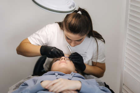 Beautician making eyelash lamination procedures for young model. Modern eyelash care procedures laminating and extension for lashes. Professional beauty studio.の写真素材